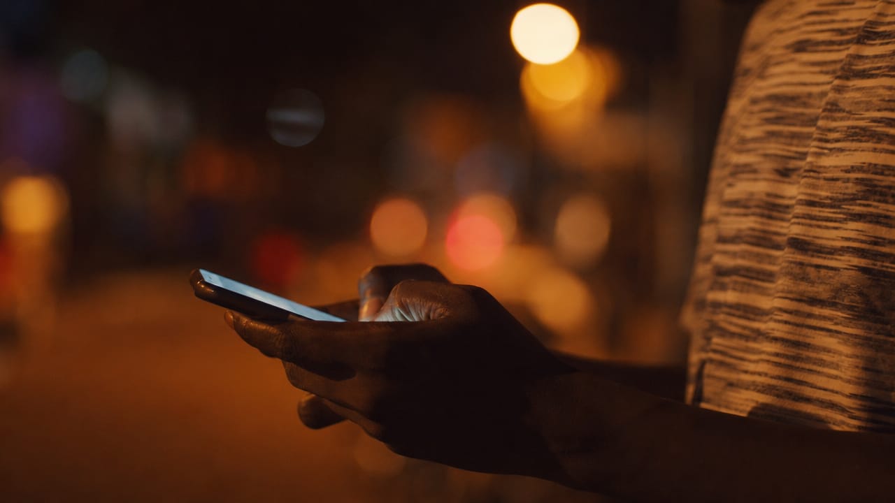 Les mains d’une personne qui écrit un message sur son téléphone, le soir en ville